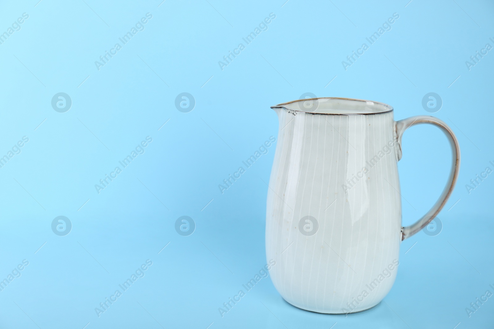 Photo of Jug of fresh milk on light blue background, space for text