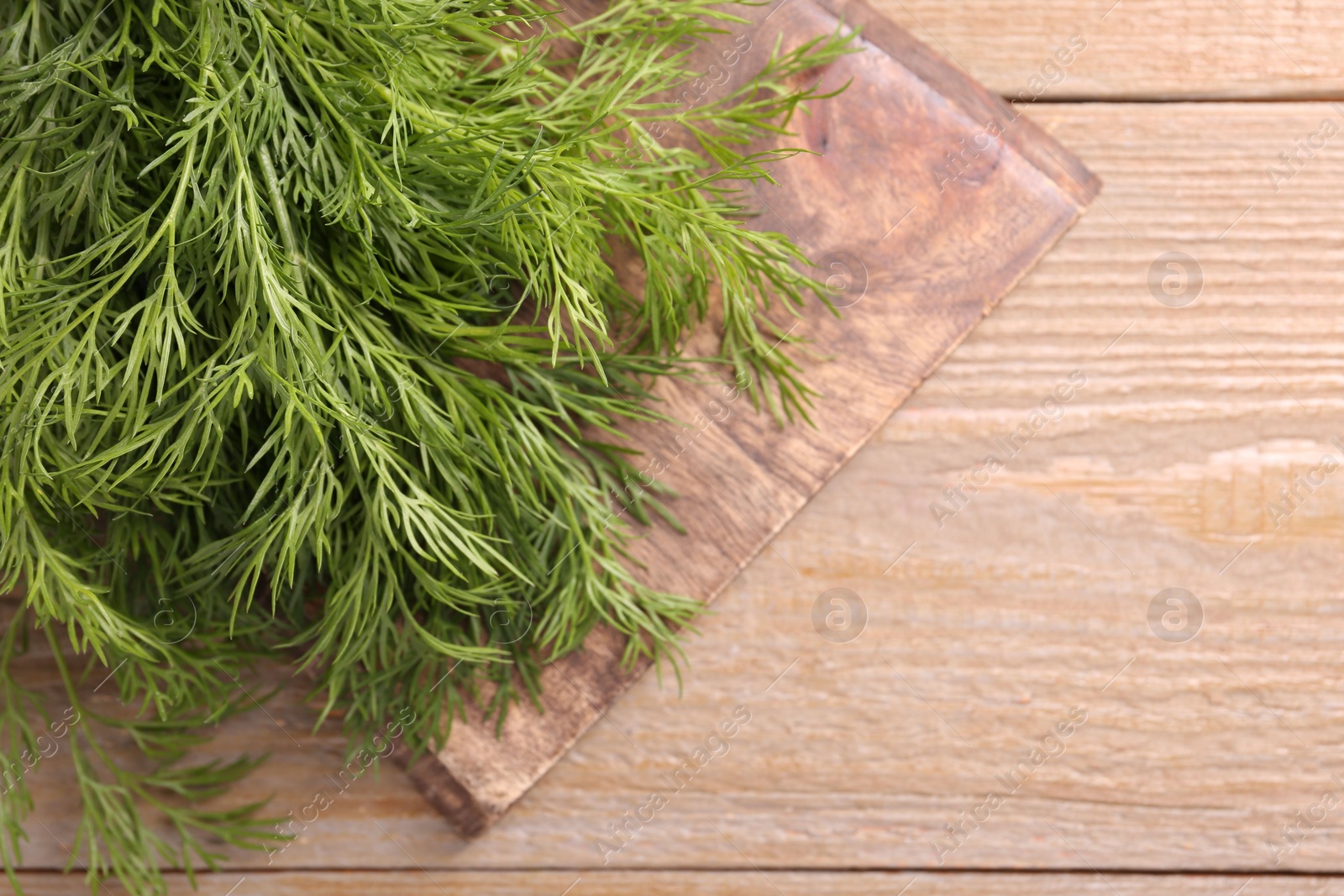 Photo of Board with sprigs of fresh dill on wooden table, top view. Space for text