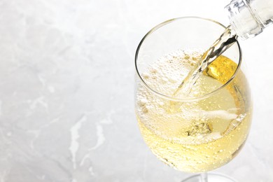 Photo of Pouring tasty aromatic wine in glass at gray marble table, closeup. Space for text