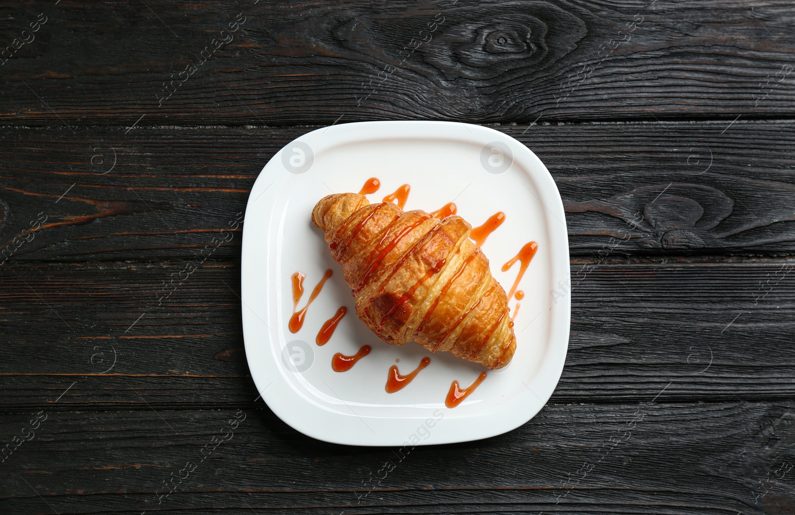 Photo of Plate of tasty croissant with jam on dark wooden background, top view. French pastry