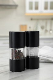 Photo of Salt and pepper mills with napkin on white marble table in kitchen