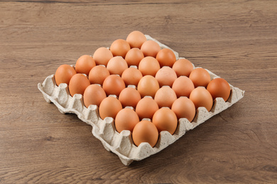 Photo of Raw chicken eggs in carton tray on wooden table