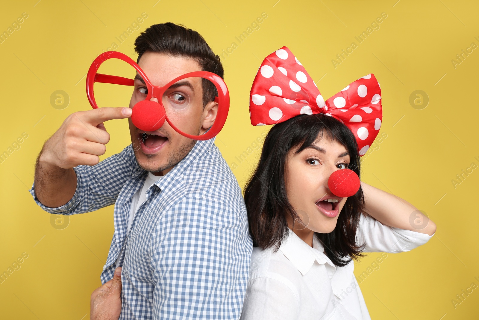 Photo of Couple with funny accessories on yellow background. April fool's day