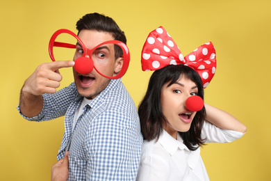 Couple with funny accessories on yellow background. April fool's day