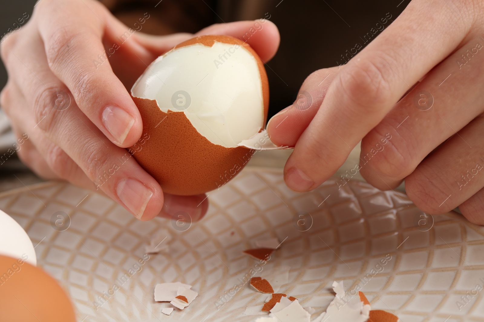 Photo of Woman peeling boiled egg over plate, closeup