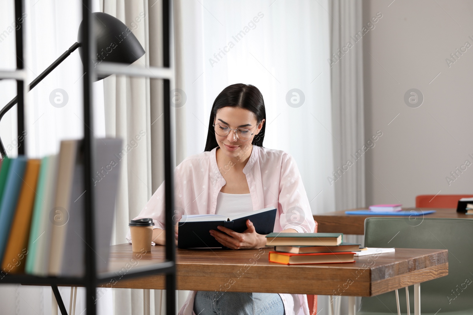 Photo of Young woman reading book at table in library