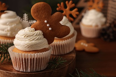 Photo of Tasty Christmas cupcake with gingerbread man and fir branches on wooden board. Space for text