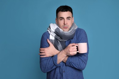 Photo of Young man with cup of hot drink suffering from fever on blue background. Cold symptoms