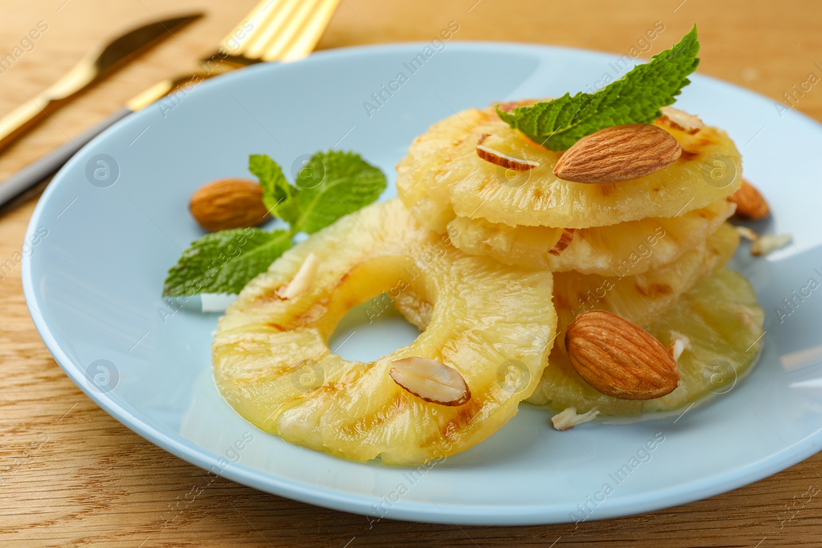 Photo of Tasty grilled pineapple slices, almonds and mint on wooden table, closeup