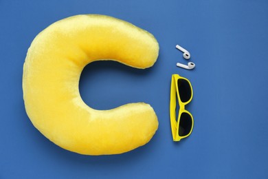 Photo of Yellow travel pillow, sunglasses and earphones on blue background, flat lay. Space for text