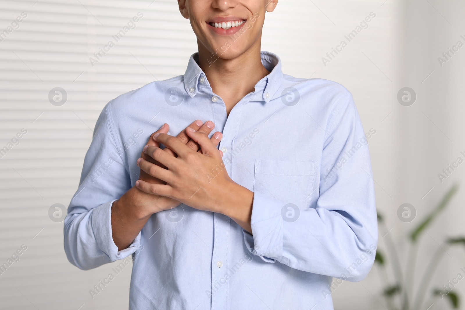 Photo of Thank you gesture. Grateful man with hands on chest indoors, closeup