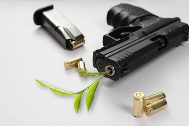 Image of Branch with green leaves, bullets and handgun on white table, closeup. Peace instead of war