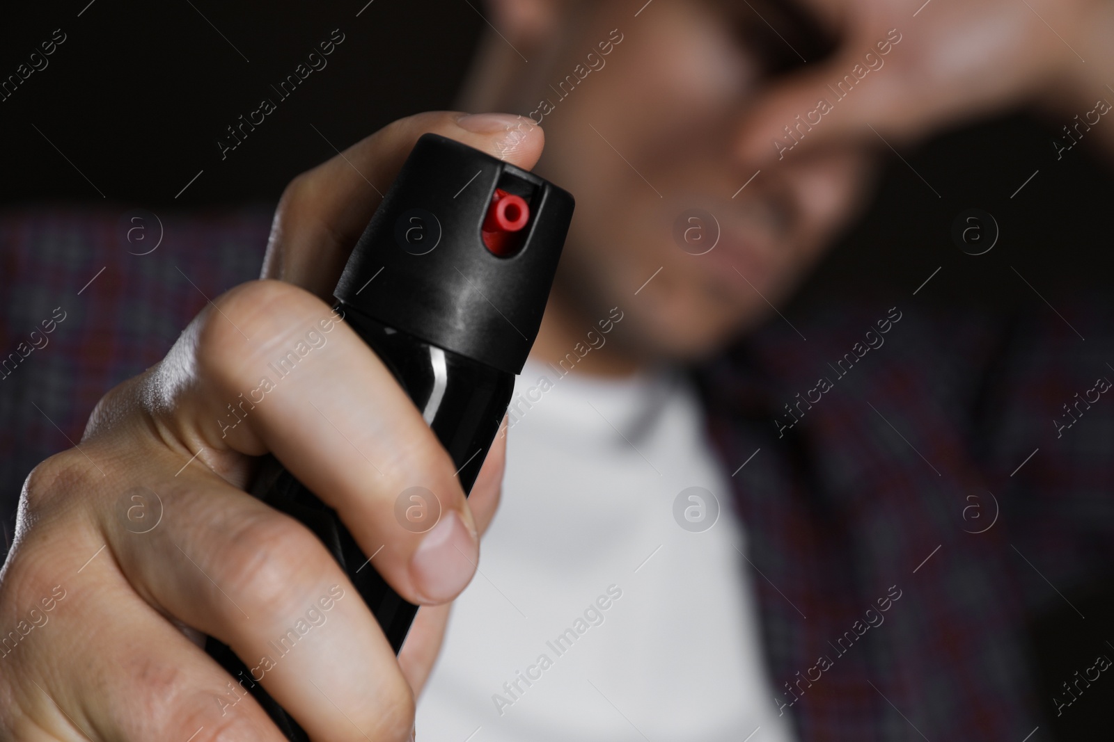 Photo of Man covering eyes with hand and using pepper spray, focus on canister