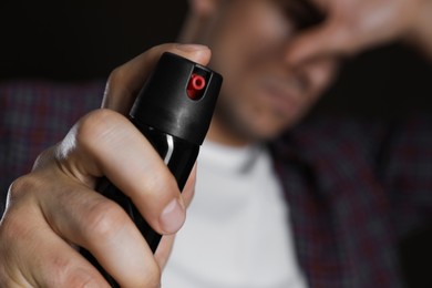 Man covering eyes with hand and using pepper spray, focus on canister