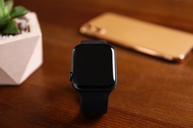 Photo of Stylish smart watch and plant on wooden table, closeup