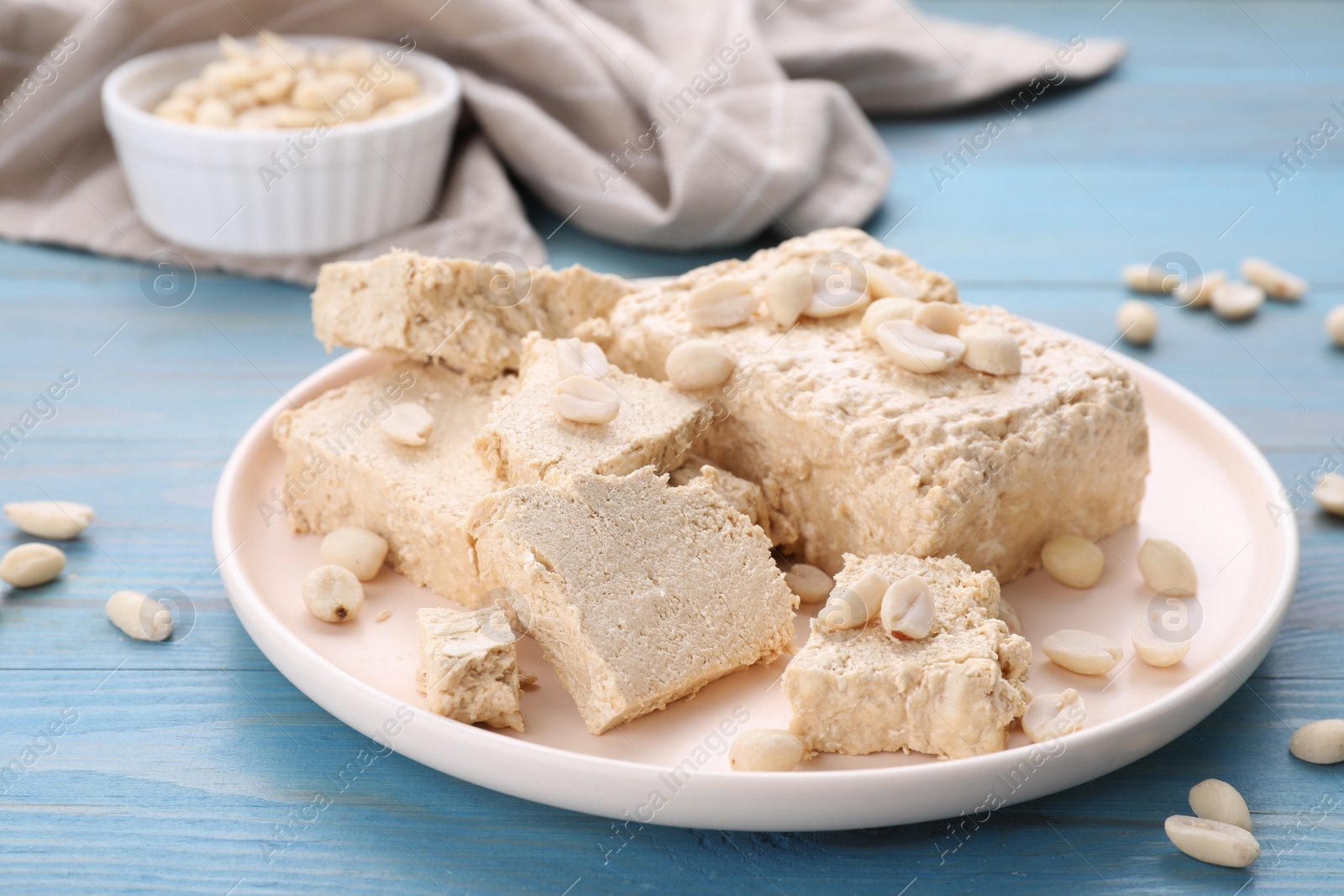 Photo of Plate with pieces of tasty halva and peanuts on light blue wooden table, closeup