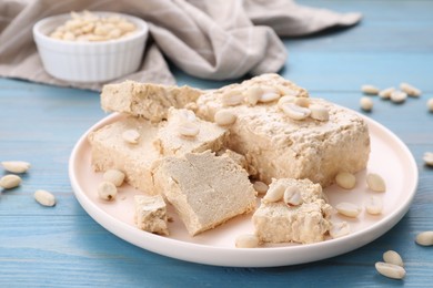 Plate with pieces of tasty halva and peanuts on light blue wooden table, closeup