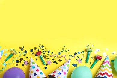 Photo of Flat lay composition with party hats, balloons and confetti on yellow background, space for text. Birthday decor