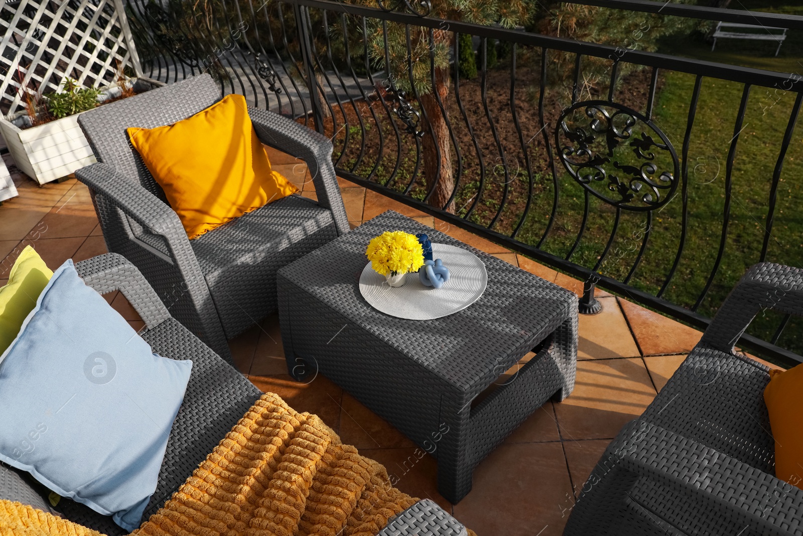 Photo of Colorful pillows, soft blanket and yellow chrysanthemum flowers on rattan garden furniture outdoors