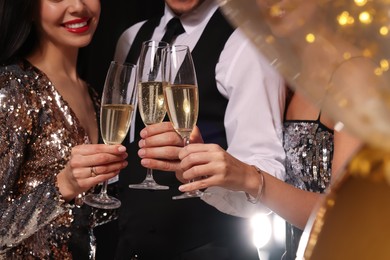 Photo of Friends with glasses of sparkling wine celebrating New Year on black background, closeup