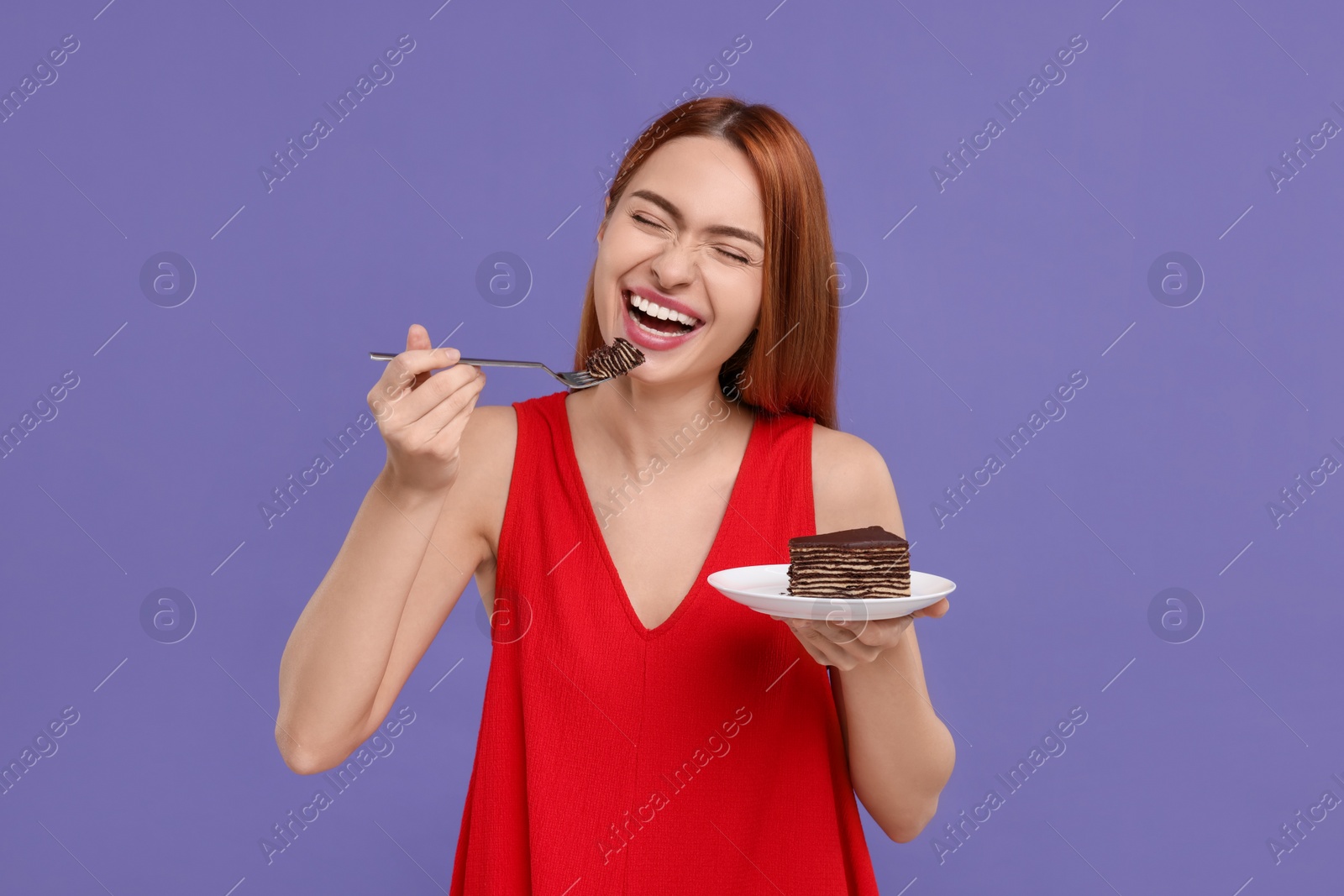 Photo of Young woman eating piece of tasty cake on purple background