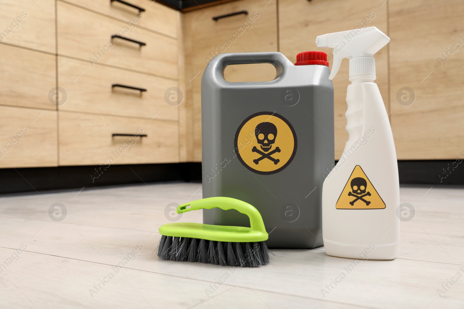 Photo of Bottles of toxic household chemicals with warning signs and brush on floor indoors, space for text