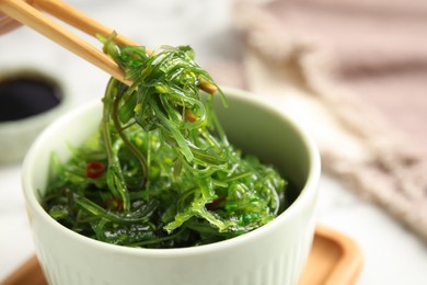 Photo of Chopsticks with Japanese seaweed salad in bowl on table, closeup