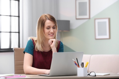 Photo of Young woman working with laptop at desk in home office