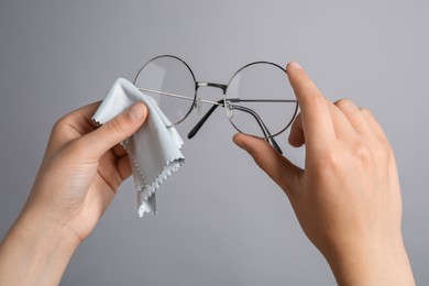 Photo of Woman wiping her glasses with microfiber cloth on grey background, closeup