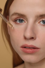 Photo of Woman applying essential oil onto face on beige background, closeup