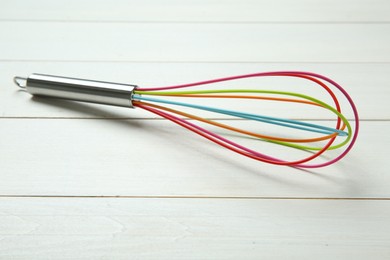Photo of One colourful whisk on white wooden table