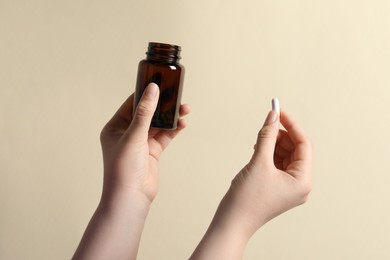 Photo of Woman holding pill and bottle on beige background, closeup