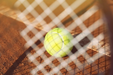 Photo of Tennis ball on clay court, view through racket