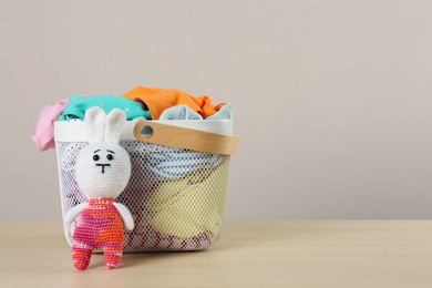 Photo of Laundry basket with different children's clothes and toy on wooden table. Space for text