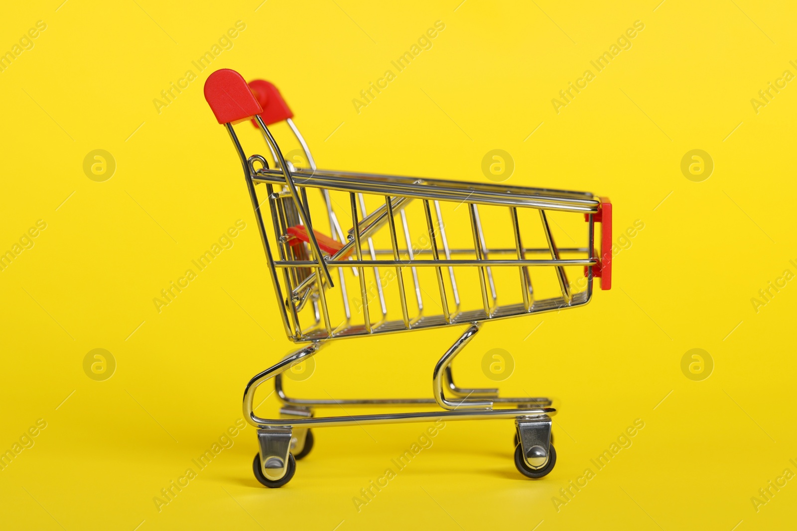 Photo of Small metal shopping cart on yellow background