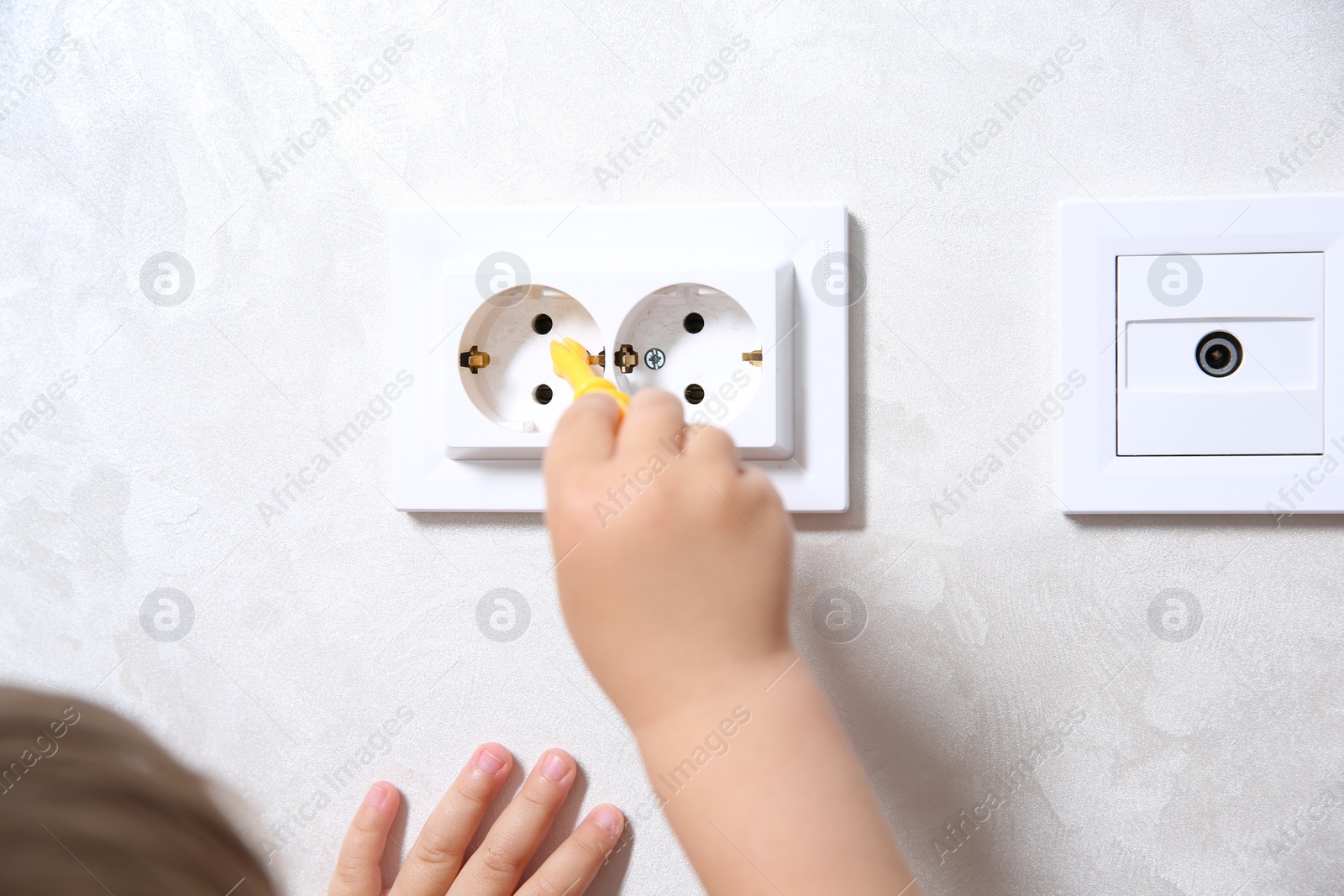 Photo of Little child playing with toy screwdriver and electrical socket at home, closeup. Dangerous situation