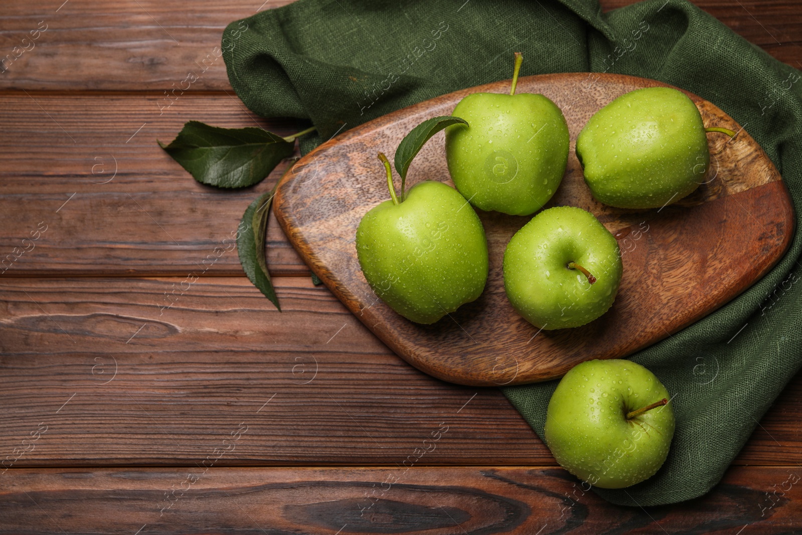 Photo of Ripe green apples with leaves and water drops on wooden table, flat lay. Space for text