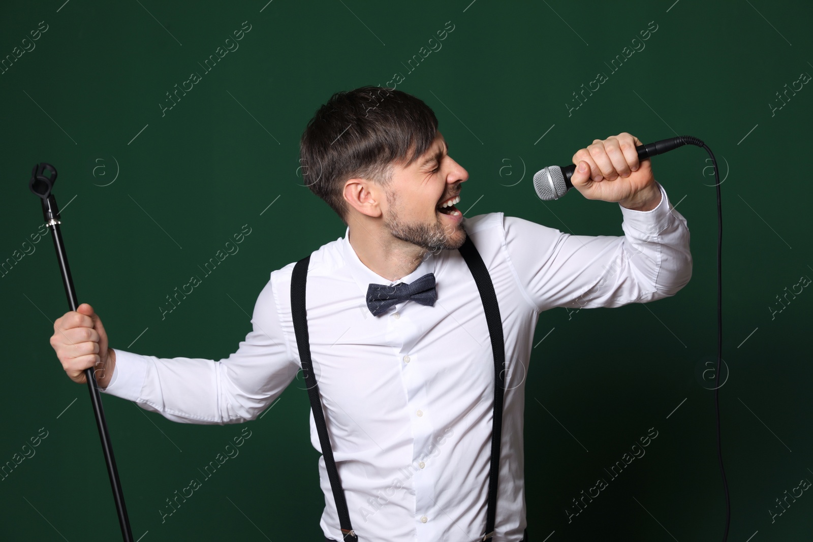 Photo of Handsome man in formal clothes singing with microphone on color background