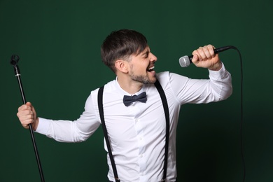 Handsome man in formal clothes singing with microphone on color background