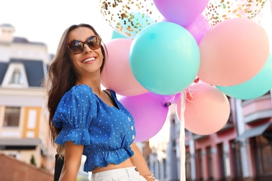 Photo of Beautiful young woman with color balloons on city street