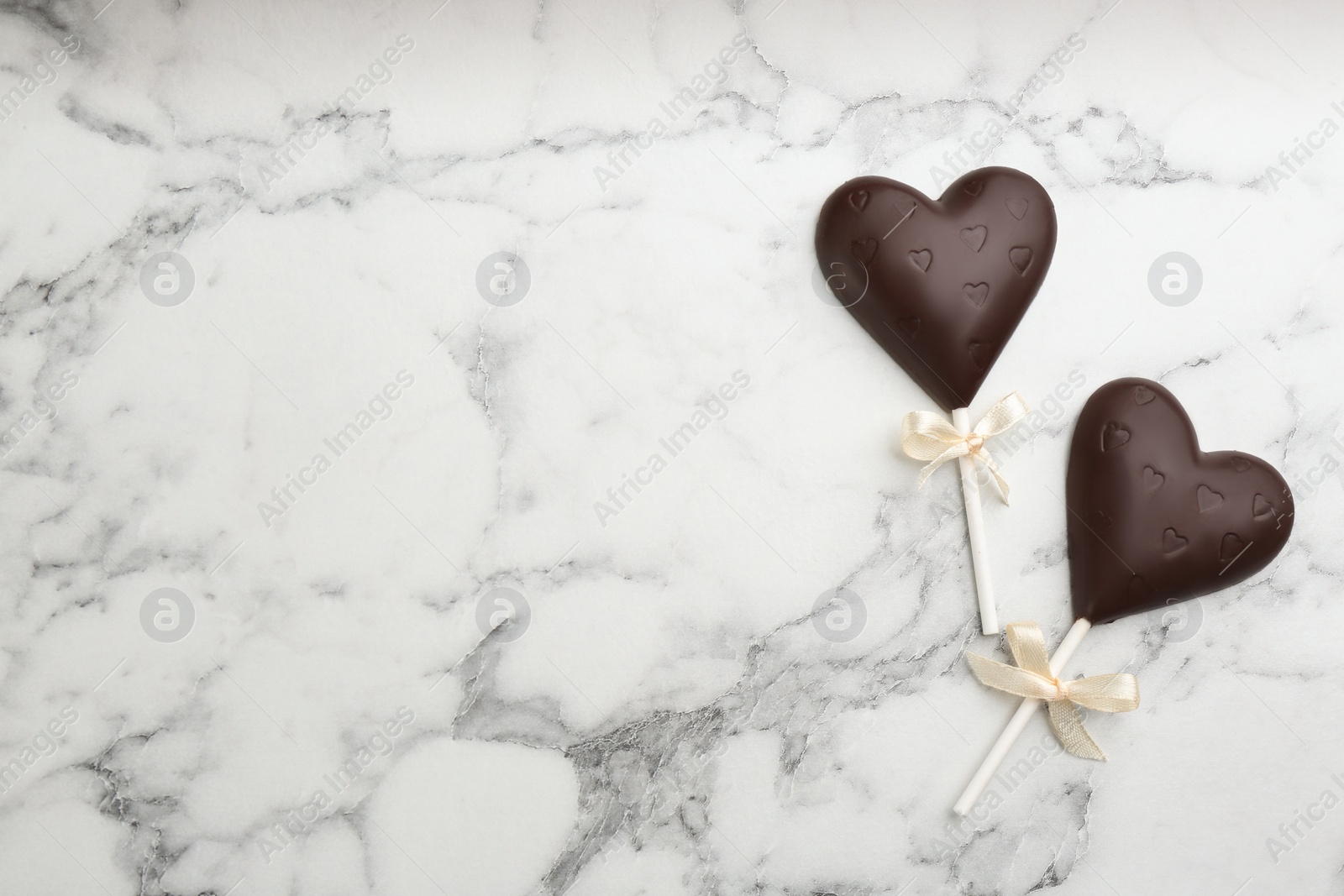 Photo of Chocolate heart shaped lollipops on white marble table, flat lay. Space for text