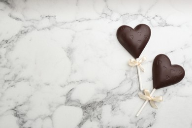 Photo of Chocolate heart shaped lollipops on white marble table, flat lay. Space for text