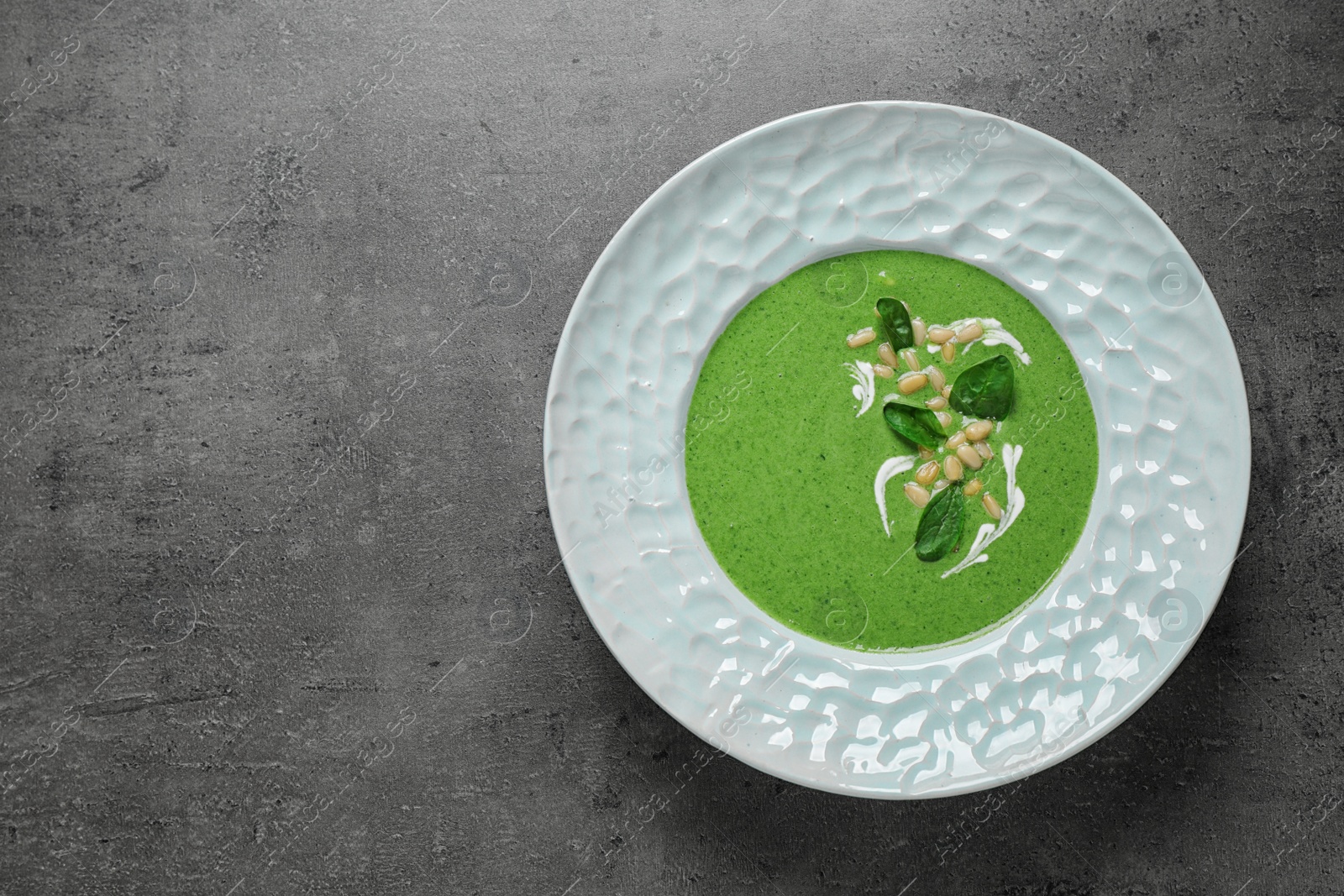 Photo of Plate of healthy green soup with fresh spinach on grey table, top view. Space for text