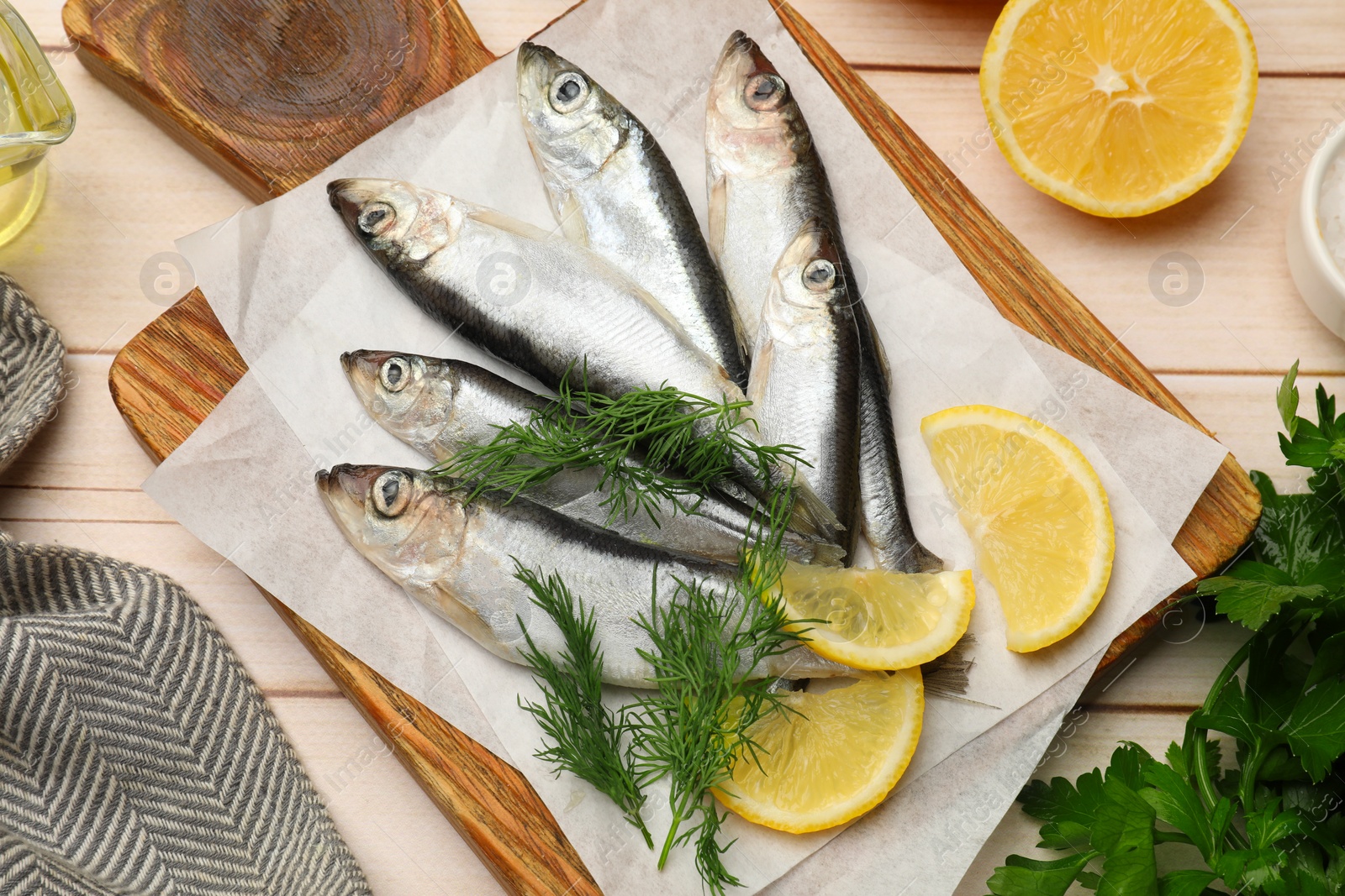 Photo of Fresh raw sprats, lemon and dill on light wooden table, flat lay