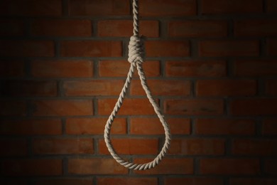 Rope noose with knot hanging near brick wall