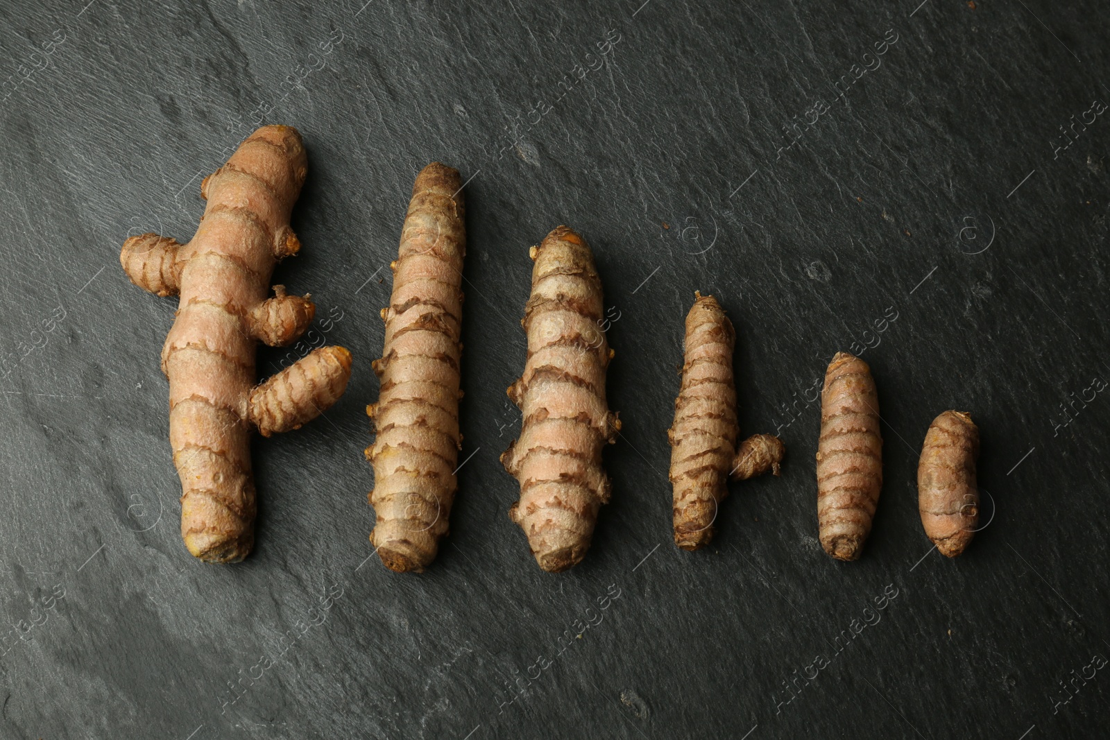 Photo of Many raw turmeric roots on black textured table, flat lay