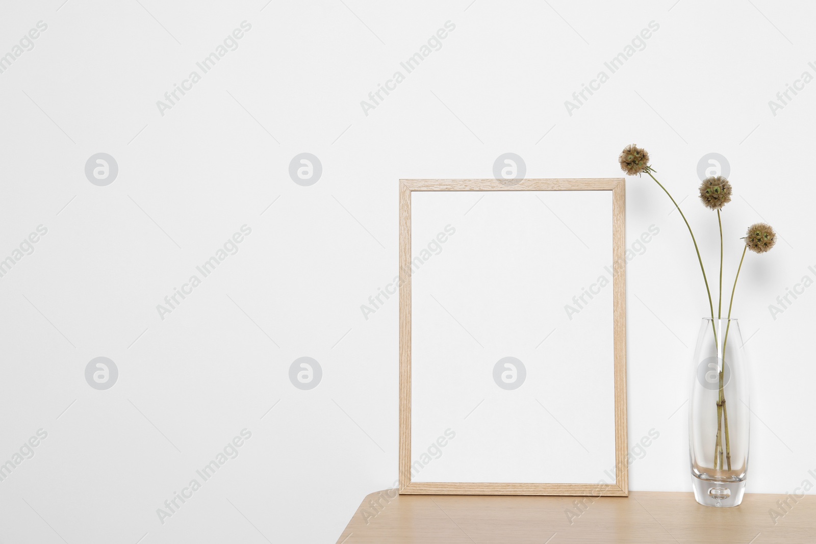 Photo of Empty photo frame and vase with dry decorative flowers on wooden table. Mockup for design