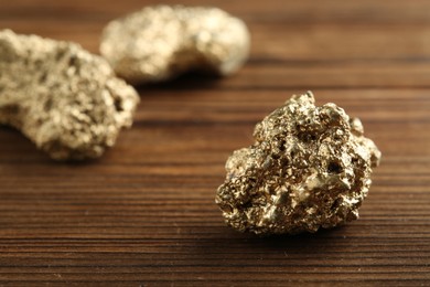 Shiny gold nugget on wooden table, closeup. Space for text