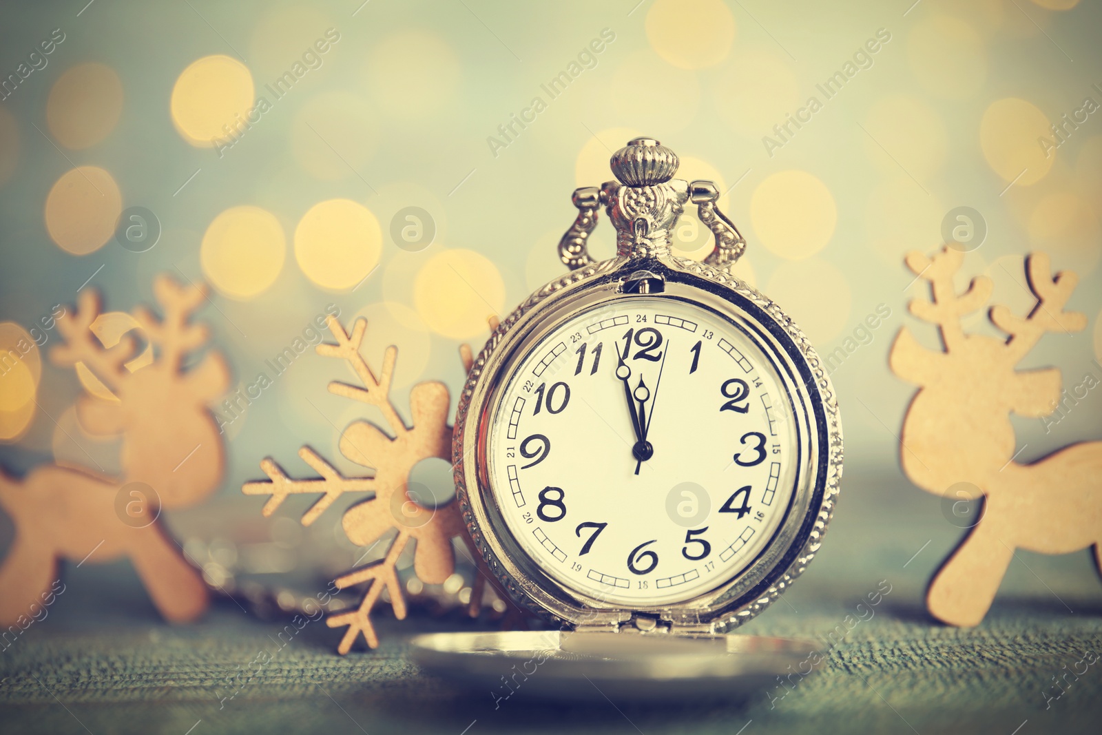 Photo of Pocket watch and festive decor on table against blurred lights. New Year countdown