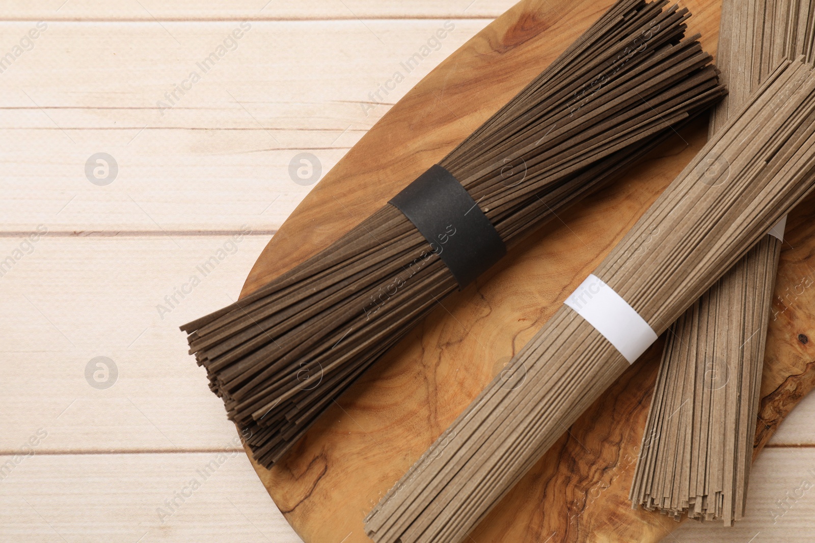 Photo of Uncooked buckwheat noodles (soba) on light wooden table, top view